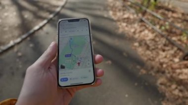 NEW YORK, ABD - 8 ARALIK 2024: Güpegündüz huzurlu bir park yolunda yürürken doğru navigasyon için akıllı telefonu kullanmak