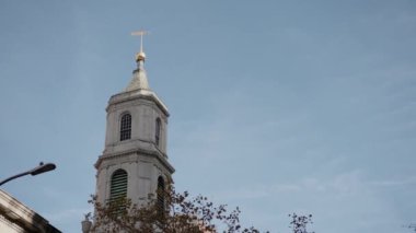 Çağdaş şehir mimarisinin ortasında haçla taçlandırılmış bir kilise kulesinin çarpıcı görüntüsü