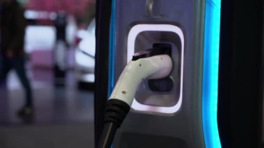 Bu resim, şarj istasyonuna sıkıca bağlı olan elektrikli bir aracın detaylı bir yakın çekimini gösterir.
