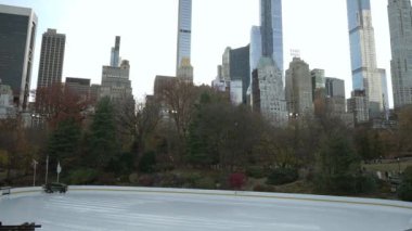 NEW YORK, ABD - 29 Kasım 2024: Central Park 'ta buz pateni pisti ve arka planda yüksek gökdelenlerin yer aldığı sakin bir kış manzarası.