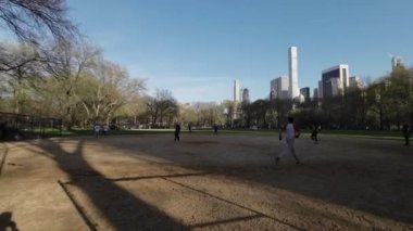 NEW YORK, ABD - 30 Mart 2024: Oyuncular enerjik bir beysbol maçına hevesle katılıyorlar Parlak, açık mavi gökyüzü altında manzaralı bir parkta