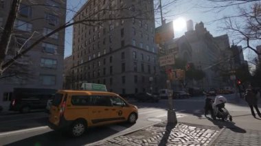NEW YORK, ABD - 8 Aralık 2024: Parlak sarı bir taksisi, hareketli binaları ve güneş ışığının tadını çıkaran yayaları olan canlı bir şehir caddesi
