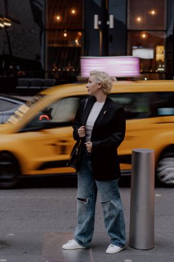 Parlak sarı bir taksi geçerken, hareketli ve canlı bir şehirde büyük bir güvenle poz veren şık bir şahıs. New York 'lu Kadın.