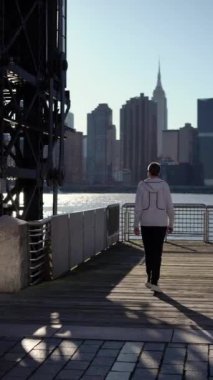 Huzurlu ve düşünceli bir şekilde rıhtım boyunca yürüyüp ikonik New York siluetine bakan bir insan.