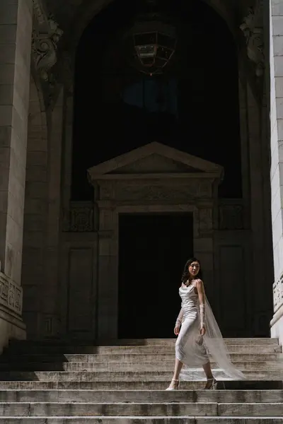 Şık bir elbise içinde muhteşem bir gelin büyük bir mimari arkaplanda akıcı bir perdeyle zarifçe poz verir..