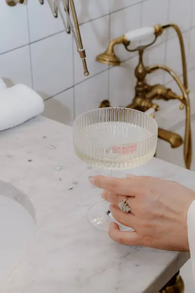 Şampanya bardağını zarif bir şekilde tutan bir el müsrif bir banyoda mermer bir lavabonun yanında, lüks bir şekilde yayılıyor.