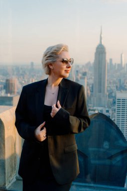 Şık ve şık bir kadın, New York 'un nefes kesen görkemli siluetine hayran kalarak çatıda duruyor.