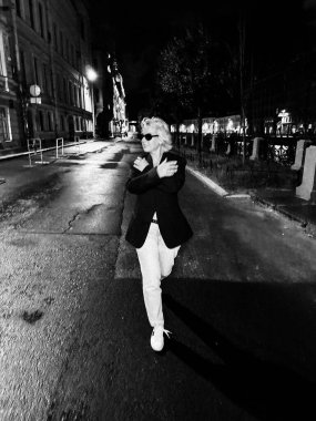 Şık bir birey, hareketli bir gecede loş bir şehir caddesinde rahatça dolaşır. Şehirde Şık ve Şık Bir Gece Yürüyüşü