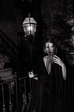 Örtülü bir kadının büyüleyici siyah beyaz portresi hem gizemi hem de zarafeti eşsiz bir şekilde çağrıştırıyor. Cadılar Bayramı cadı kostümü.