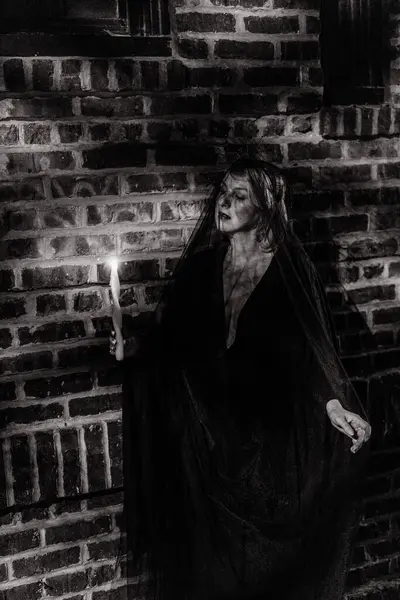 Ürkütücü ve büyüleyici bir portre, loş mum ışığı ve peçeyle. Bir mum ile yalnız bir figür rahatsız edici bir görüntü, karmaşık dokulu tuğla arka plan karşı. Cadılar Bayramı Cadısı.