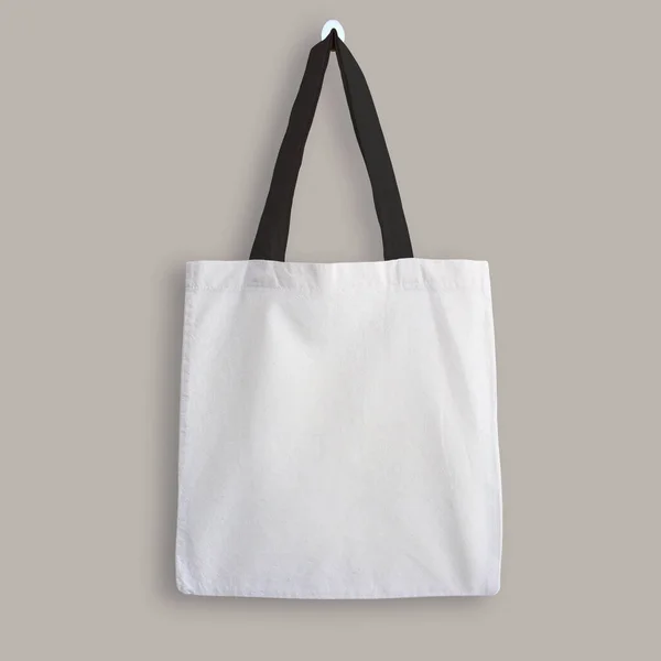 White blank cotton eco tote bag with black straps, design mockup. Shopping bag hanging on wall.