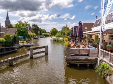HEEG, NETHERLANDS - 6 Temmuz 2023: Heeg, Friesland, Hollanda merkezindeki kanalın rıhtımındaki terasta dinlenen insanlar