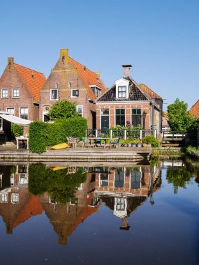 Hindeloopen, Netherlands - May 14, 2024: Houses on quayside of Zijlroede canal reflecting in water on cloudless sunny day, Friesland clipart