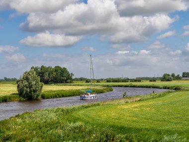 Reitdiep, Hollanda - 4 Temmuz 2024: Groningen kırsalındaki Reitdiep kanalında yelkenli yelkenli kanalı çevresi tarım arazisi, çayır ve manzaralı kırsal bölgelerle çevrili