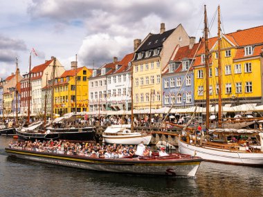 Kopenhag, Danimarka - 8 Ağustos 2024: Nyhavn Kanalı turistlerle dolu rıhtım kenarı, insanlarla dolu bir tur botu ve zirve sezonunda tarihi konak evleri