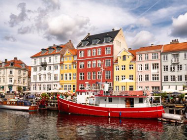 Kopenhag, Danimarka - 8 Ağustos 2024: Renkli Nyhavn kanal evleri, demirli tekneler, insanlarla dolu rıhtım kenarı, Kopenhag, Danimarka, yaz mevsimi