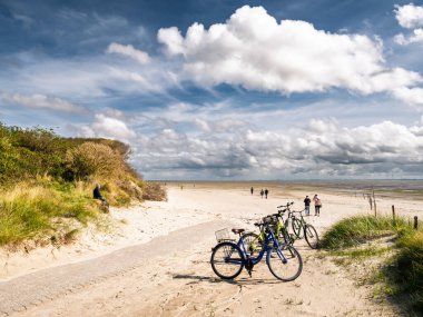 Osterhook, Doğu Frizya adası Langeoog, Aşağı Saksonya, Almanya 'da plajda parkedilmiş bisikletli yürüyüş yolu, Wadden Denizi manzarasının alçak gelgitte keyfini çıkaran insanlar