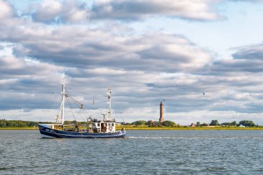 Norderney, Almanya - 14 Şubat 2024: Wadden Denizi 'ndeki balıkçı teknesi Doğu Frizya adası Norderney, Aşağı Saksonya' daki deniz fenerini geçiyor