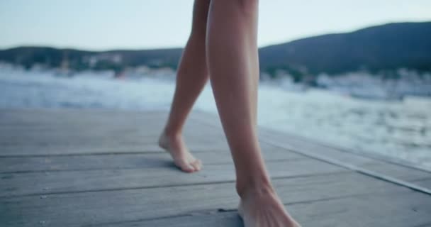 木製の桟橋で女性の足を歩いて閉じます 若い痩せっぽちの女性がビーチで木のボードウォークを裸足で歩く 地中海の休暇の概念 — ストック動画