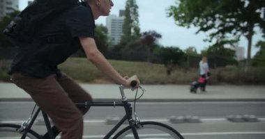 Şehirdeki banliyö bisikletçisinin yan görüntüsü. Genç adam işe giderken bisiklet yolunda basit bir şehir bisikleti sürüyor. İki bisikletçi ayrılan bikelane üzerinde birbirini solluyor. 