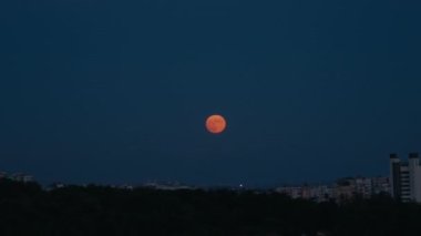 Kırmızı ay tutulması şehrin üzerinde yükseliyor. Kırmızı ya da turuncu renkte dolunay apartmanların üzerinde yükseliyor.. 