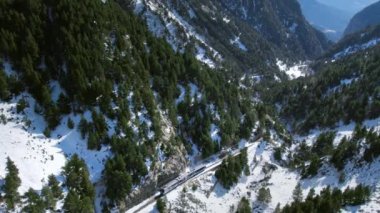 Cinematic aerial drone shot following touristic train in snow mountain landscape. Vacation adventure cold winter scenery. 