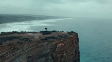 Aerial drone shot of couple stand on top of camper van, hold hands and look out into distance. Inspiring vanlife offroad adventure. Urban nomads living offgrid in overlanding vehicle