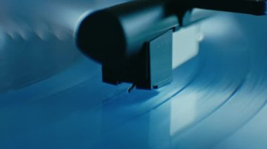 Close up of turntable stylus on the silky blue vinyl spinning on the vintage record player. Stylish retro music equipment in modern design. 