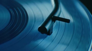 Super close up on turntable stylus touching vintage blue vinyl. Tone arm with needle, cartridge and stylus play music. 