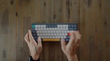 Top view of a software engineer hands using hipster portable devise at work in the office. Communications with business team via emails from home. Stylish computer keyboard on the wooden table. 