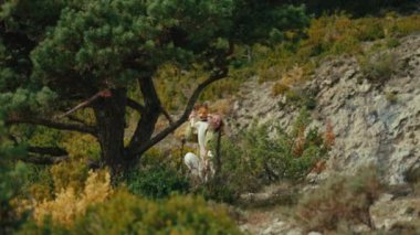 Woman with dog sit on the hill surrounded by nature. Funny animal look at the camera and waving. Colorful landscape, autumn vacation with pet. Joy of freedom and outdoor lifestyle.