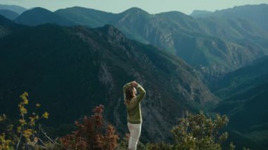 Cinematic woman in traditional sweater on top of mountain hill look at forest valley. Young hiker enjoy outdoor lifestyle. Majesty of nature. Travel concept.