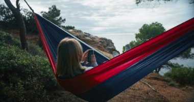 Yeşil tepedeki bir hamakta, kadın telefonunu ağaçlar ve mavi denizle çevrili bir şekilde kaydırıyor. İnternet parmaklarının ucunda olmasına rağmen dinlenmeye, meditasyon yapmaya ve doğası gereği barışçıl salıncaktan zevk almaya vakit buluyor..