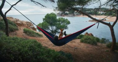 Adam hamakta, orman sahilinde köpekle yatıyordu. Yaz güneşinin tadını çıkarıyor, meditasyon yapıyor ve tamamen rahat bir şekilde mavi denizin muhteşem manzarasına hayran kalıyor.. 