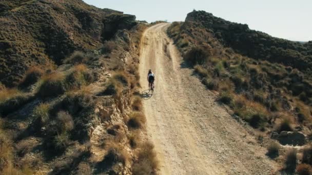 プロのアスリートが苦しんでおり 砂漠の景色の美しさで上り坂の砂利の自転車のサイクリングの挑戦にかかります 山の平和的な景色は 冒険とさまよう欲望のスポーツマンの感覚を刺激します — ストック動画