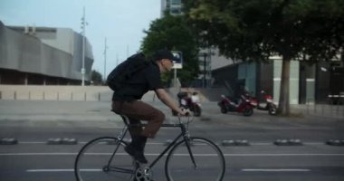 Günlük kıyafetlerle gezen genç bir adamın güvenli bisiklet yolunda bisiklet sürdüğü güneşli bir sabah fotoğrafı. Bisikletle şehir içi taşımacılık kavramı. Yeşil banliyö rutini