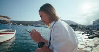 Genç seyahat blogcusu sosyal medya bloglarında veya Akdeniz limanında içerik oluşturmada akıllı telefon kullanıyor. Yaz tatili ve sosyal medya işi kavramı