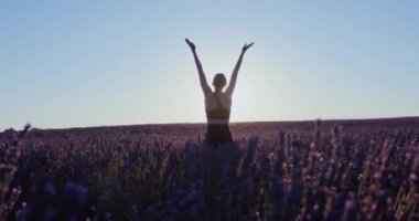 Kadın blogcu, güneş doğarken pembe ve mor lavanta tarlalarında yoga yapıyor. Rüya gibi ve ilham verici bir sabah. Özgür ve mutlu bir kadın spor giysileri içinde esniyor. Meditasyon konsepti. 