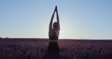 Provence 'deki pembe ve mor lavanta tarlalarında gün doğumunda bir kadın rüya gibi spor kıyafetleriyle yoga asanas yapar. İlham verici meditasyon pratiği. El kamerasıyla. Lens üzerinde güneş parlıyor.. 