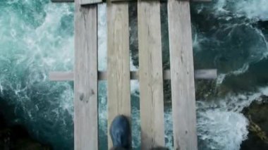 Yürüyüş ayakkabıları sürüsü hızlı ve mavi dağ suyu akıntısı üzerinde yürür. Destansı buzul nehri ve asma ahşap köprü. İskandinav bayramı. Ormanda tehlikeli patikada yürüyüş macerası.