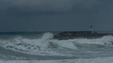 Karanlık gökyüzü ve dalgaların dalgalanan sulara çarpması doğanın tehlikeli güzelliğini gösteriyor. Bulutlu gökyüzü bir fırtınanın habercisidir. Martılar denizin üzerinde avlanıyor. İklim değişikliği. 