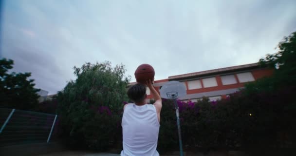 バスケットボール選手は輪にボールを撃ち リムに集中します 屋外の裁判所で撮影された映画の夜 成功を達成するための決意と努力 標的の目 — ストック動画