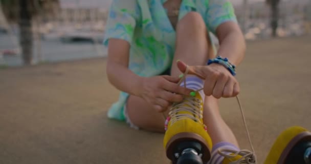 一名年轻女子笑着把鞋带绑在复古黄色滚筒上 坐在一座海滨城市的一个码头上 阳光灿烂 海风吹拂着她的头发 五彩缤纷的夏装 — 图库视频影像