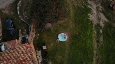 Bikinili ve bereli genç bir kadının ahşap ısıtılmış jakuzide mavi suyla rahatlarken en üstten drone görüntüsü. Doğal beslenme jakuzisi ya da açık hava banyosu. Glamping dış kaplıca inziva yeri