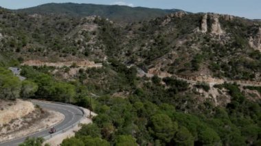 Costa Brava sahilinde nefes kesen dağlarla çevrili bir hava aracı görüntüsü. İki kişi bir yılan boyunca motosiklet sürüyor. Idyllic yaz tatili ya da hafta sonu. Turizm beldesi. 