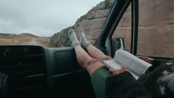 旅行者の女性は ダッシュボードの足で旅行ガイドや小冊子を見て スカンディナヴィア ノルウェー スウェーデンの周りの壮大なロードトリップでキャンパーバンを運転します 北欧の冒険 — ストック動画