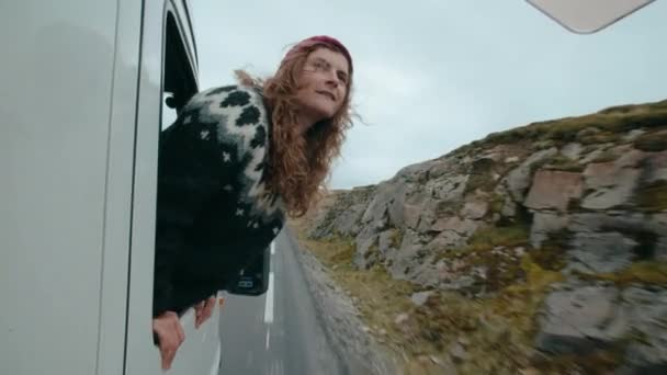 在欧洲北部 在电影般的公路旅行中 由于好奇的游手好闲的旅行冒险家 女人从车窗或野营面包车里探出头来 看外面 随风飘荡 在路上有一种自由的感觉 — 图库视频影像
