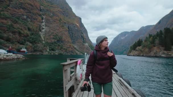 女性の旅行写真家は 景色を望む周辺の桟橋を歩いています 秋のノルウェーのフィヨルド色 アドベンチャーブロガーをインスパイアし ソーシャルメディアや旅行代理店のコンテンツを作成する — ストック動画