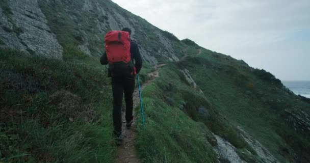 赤いバックパックとトレッキングポールを持つ若い旅行者は 海のビーチの近くの壮大な景色の美しい山のトレイルに丘を歩きます ポルトガルの海岸巡礼 インスピレーションのムーディアドベンチャーライフスタイル — ストック動画