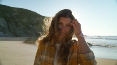 Genç bir kadının sinematik portresi kameraya gülümsüyor. Saçları yüzünden çek, kamerayla etkileşime geç. Sörf macerasının güneşli sarı gölgesi ya da otantik milenyum yolcusu. Sosyal medya etkileyiciName